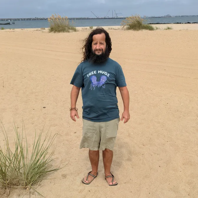 David Barbarisi standing on a beach wearing a grey 'Free Hugs' t-shirt with an octopus graphic